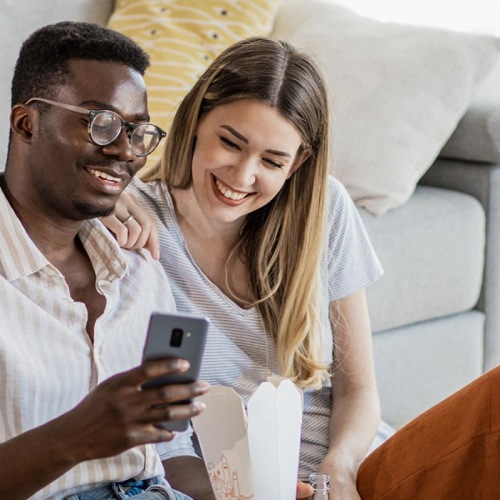 a man and woman sitting on a couch looking at a cell phone